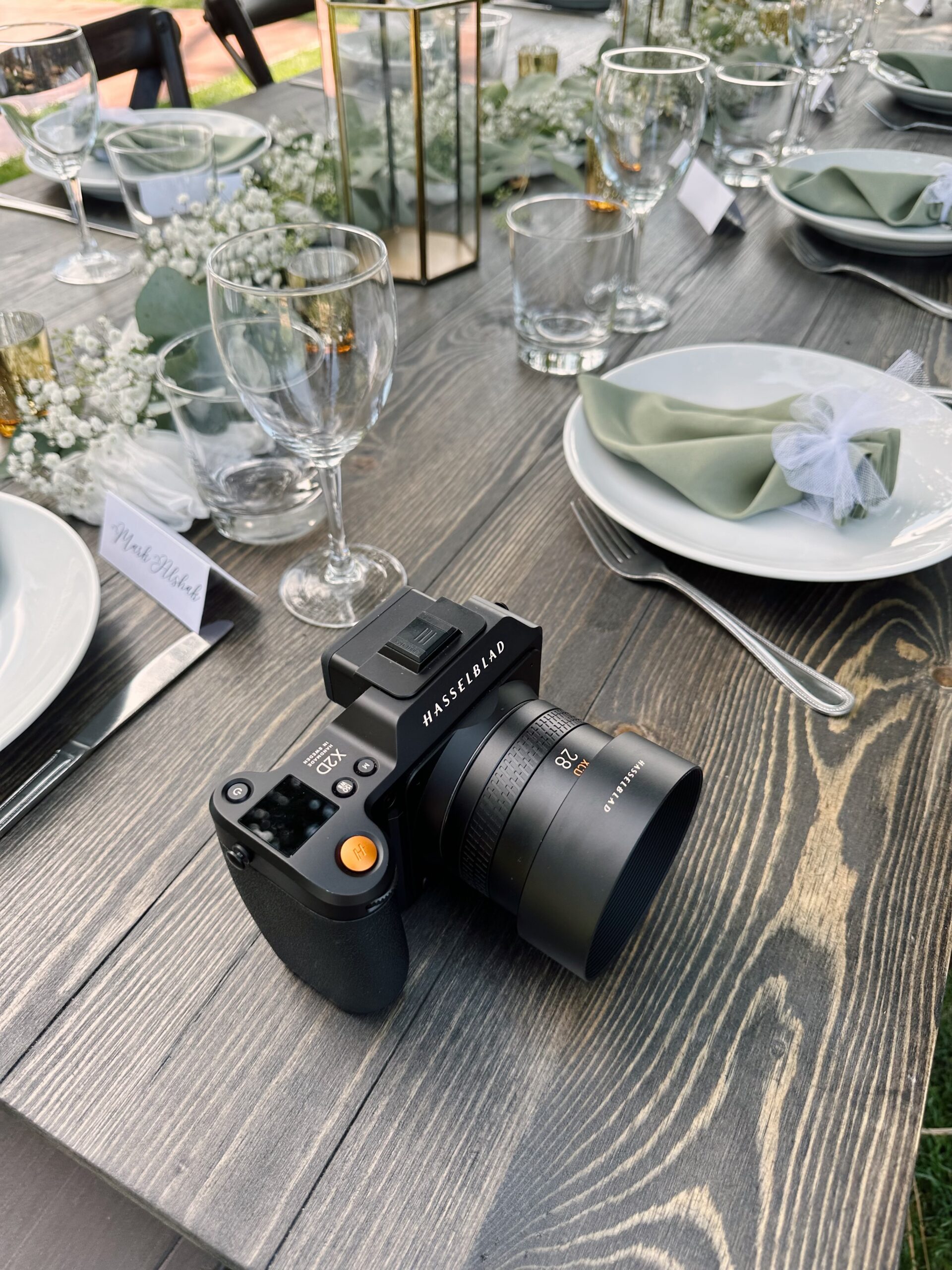 Hasselblad X2D 100C shown on a wooden table alongside an array of place settings, a table runner, white florals, and other decor.